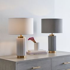 two lamps sitting on top of a dresser next to a book and a lamp shade