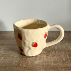 a coffee cup with strawberries on it sitting on a wooden table next to a white wall