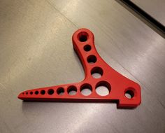 a red metal object with holes in the middle on a counter top or flooring