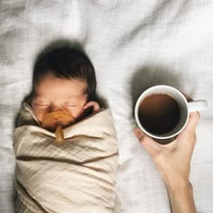 a newborn baby wrapped in a blanket next to a cup of coffee on a bed