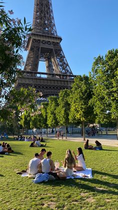 people sitting on the grass in front of the eiffel tower