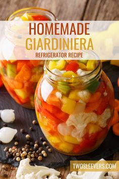 two jars filled with vegetables sitting on top of a wooden table next to garlic and pepper