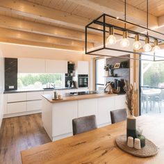 an open kitchen and dining room area with wooden flooring, white cabinetry and pendant lights hanging from the ceiling