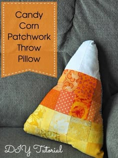 the candy corn patchwork throw pillow is sitting on a gray couch with an orange banner over it