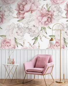 a pink chair sitting in front of a wall with flowers on it and a lamp next to it