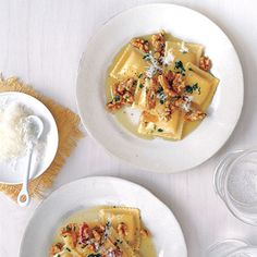 two white plates topped with ravioli covered in cheese and sauce next to empty glasses