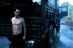 a shirtless man standing next to a truck in the rain