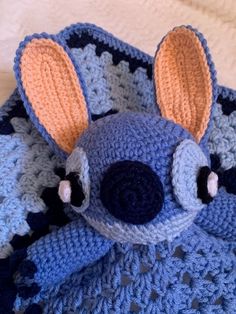 a crocheted stuffed animal laying on top of a blue and gray blanket with ears