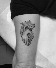 a black and white photo of two hands holding a rose tattoo on the left arm