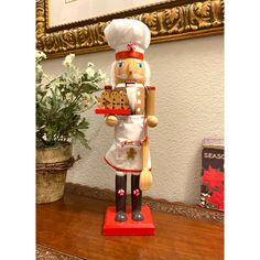 a wooden nutcracker standing on top of a table next to a potted plant