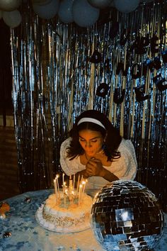 a woman blowing out candles on a birthday cake in front of disco balls and streamers