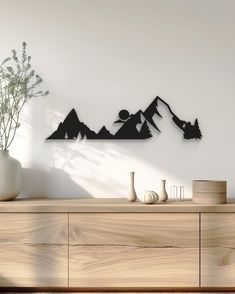 a wooden dresser topped with a vase filled with flowers next to a wall mounted art piece