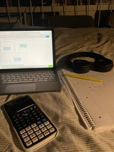 an open laptop computer sitting on top of a bed next to a calculator