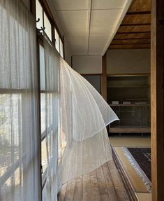 an open window with sheer curtains hanging from it's sides, in front of a wooden floor