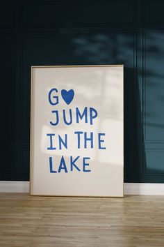 a white framed poster with the words jump in the lake on it sitting on a hard wood floor