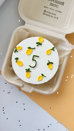 a white cake with yellow flowers on it in a box next to confetti