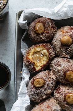 powdered sugar covered doughnuts in a metal tray with dipping sauce on the side