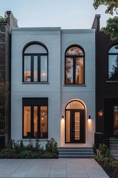 a white brick house with black trim and arched windows at the front door, along with steps leading up to the second floor