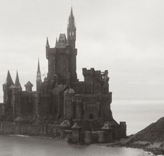 an old castle sitting on top of a hill next to the ocean in black and white