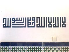 arabic writing on the wall above a toilet in a tiled room with blue and green tiles