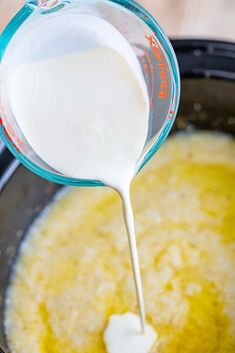 a person pouring milk into a pot filled with yellow liquid and other ingredients to make it