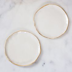 two white and gold plates sitting on top of a marble countertop next to each other