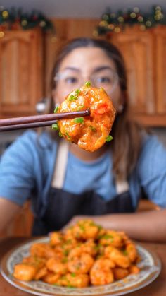 a woman holding chopsticks over a plate of food with shrimp on it in front of her face