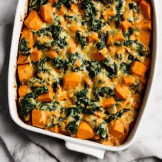 a casserole dish with sweet potatoes and spinach in it on a marble surface