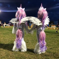 two people dressed as unicorns standing on top of a grass covered field at night