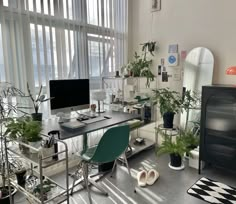 an office with lots of plants on the desk and in front of a large window