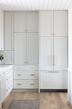 a kitchen with white cabinets and gold pulls on the doors, wood flooring and hardwood floors