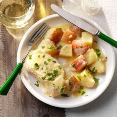 a white plate topped with fish and potatoes next to a glass of wine on top of a wooden table