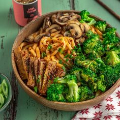 a bowl filled with noodles, broccoli and mushrooms on top of a table