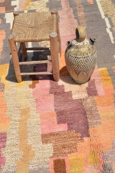 a vase sitting on top of a colorful rug next to a wooden table and chair