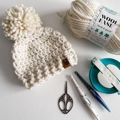 yarn, scissors and knitting needles are on the table next to a ball of yarn