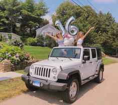 two women standing on top of a silver jeep with balloons in the shape of numbers