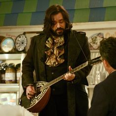 a man with long hair and beard playing an acoustic guitar in front of other people