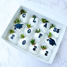 a box filled with white chocolate covered in frosting and topped with strawberries, green leaves and graduation caps