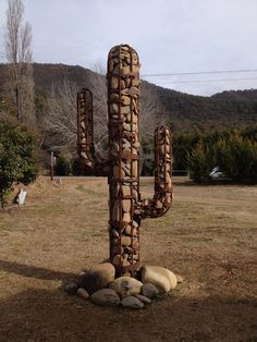 a large cactus sculpture sitting in the middle of a field next to rocks and trees