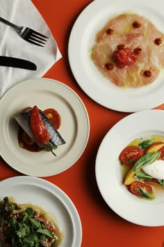 three white plates with different types of food on top of an orange table cloth and utensils