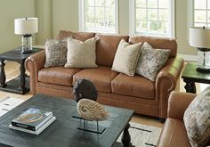 a living room filled with furniture and pillows on top of a wooden coffee table in front of two windows