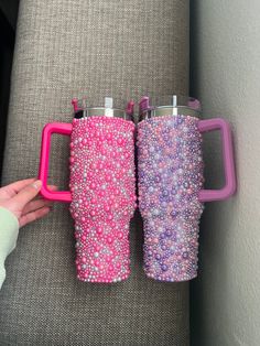 two pink and purple coffee mugs sitting next to each other on a gray couch