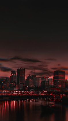 the city skyline is lit up at night with red lights in the foreground and dark clouds in the background