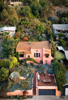 an aerial view of a pink house surrounded by trees and bushes with lots of greenery