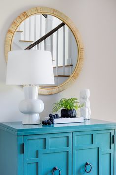 a blue dresser with a white lamp and mirror on the wall next to it in a living room