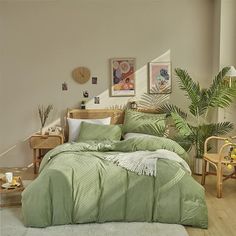 a bed with green comforter and pillows in a bedroom next to a plant on the floor