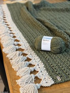 a green and white blanket sitting on top of a wooden table next to a ball of yarn