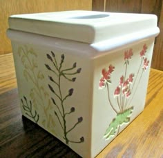 a white box with flowers painted on the side sitting on a table next to a wooden door