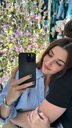 two people are taking a selfie with their cell phones in front of a flower wall