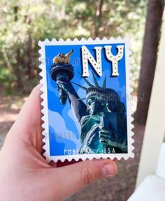 a person holding up a postage stamp with the statue of liberty in new york city